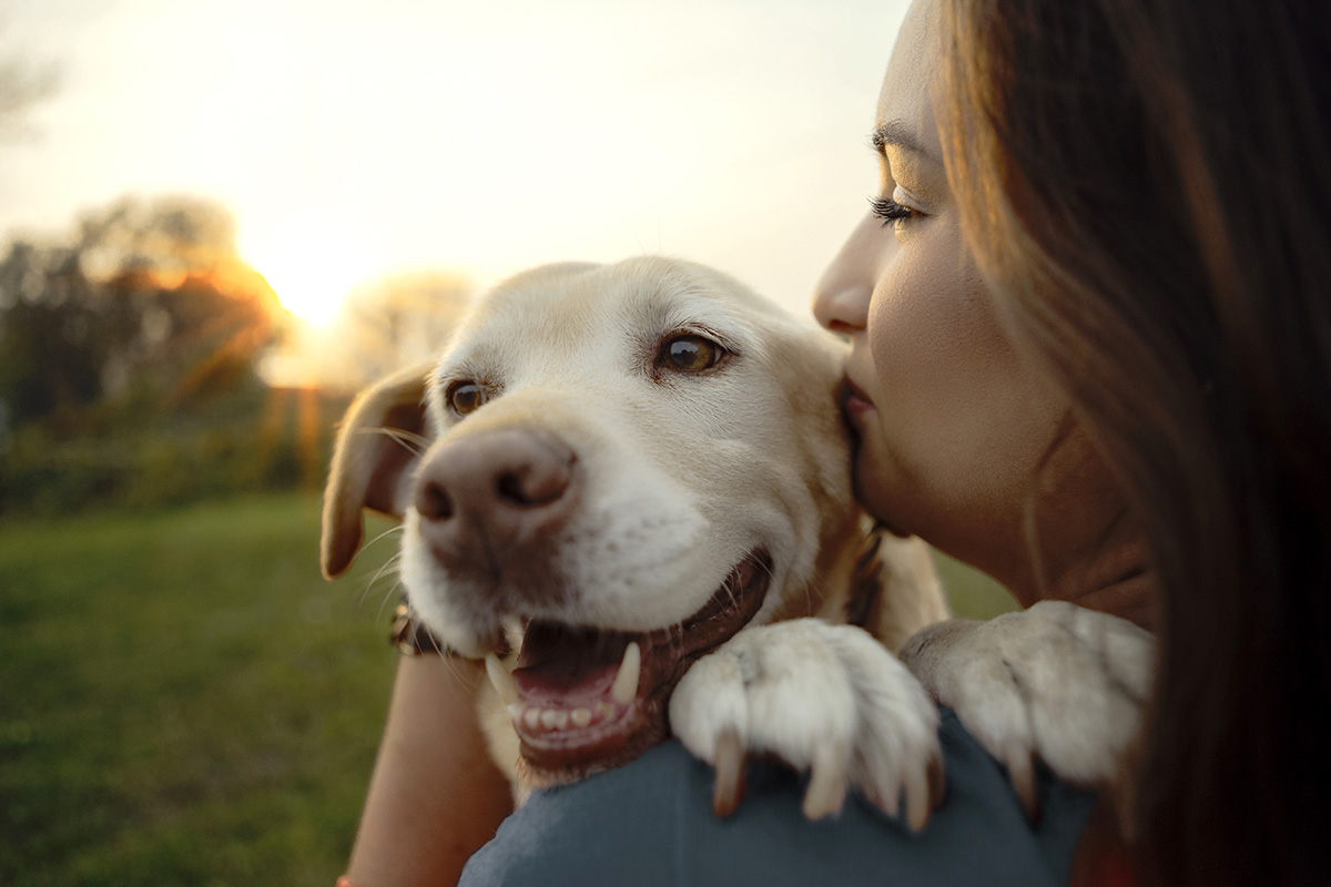 Frau kuschelt mit Hund im Abendlicht